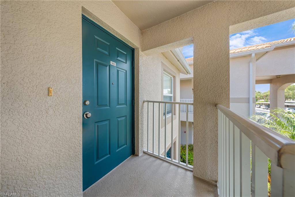 Entrance featuring a teal paneled door with polished hardware, textured stucco exterior, and a private balcony with white railings