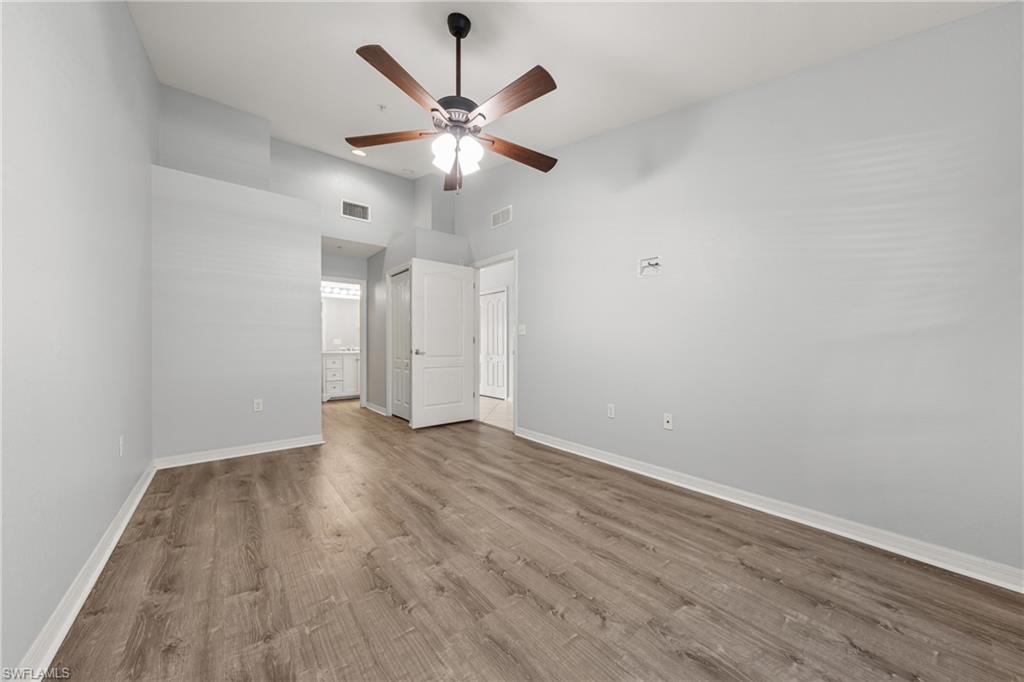 Spacious room featuring wood-finish flooring, light gray walls, and a ceiling fan with integrated lighting