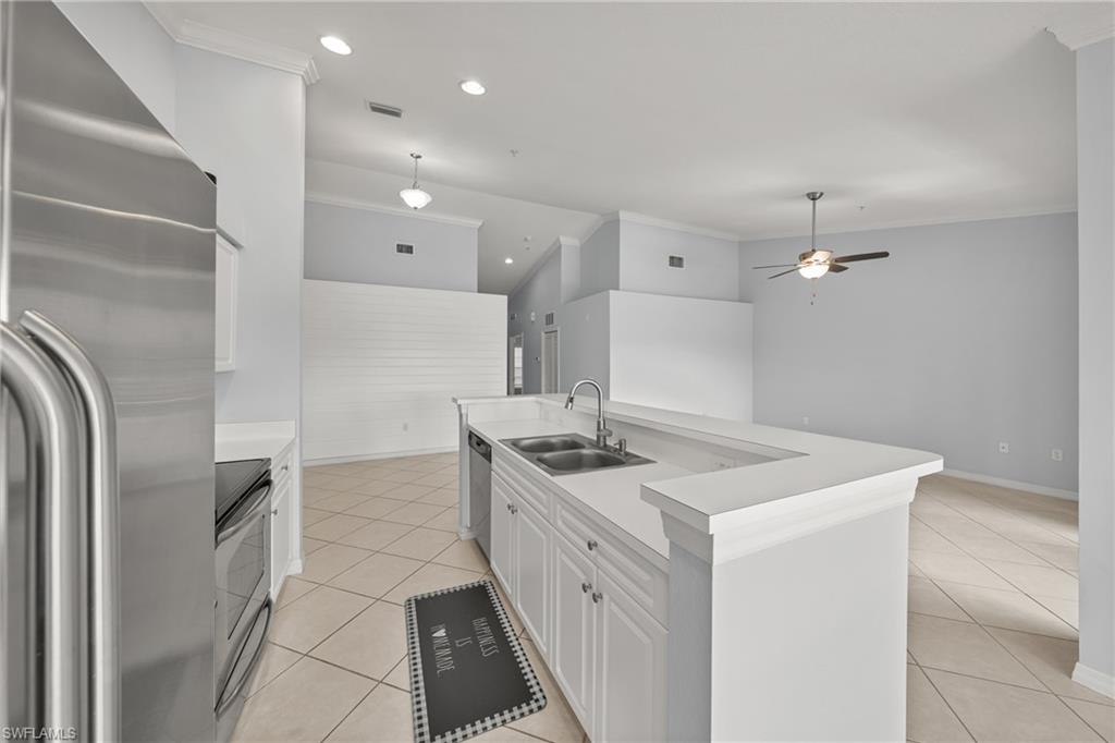 Kitchen featuring a stainless steel refrigerator, white cabinetry, a double basin sink, and a breakfast bar with white countertops