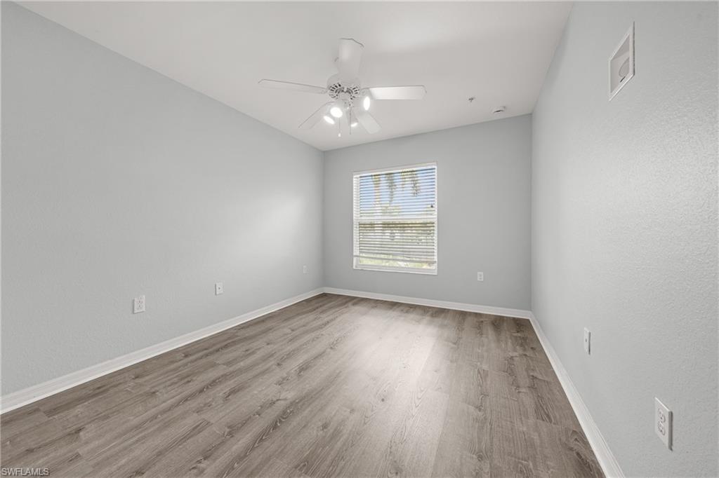 Spacious room featuring wood-finish flooring, light gray walls, a window with horizontal blinds, a white ceiling fan with integrated lighting, and white baseboards