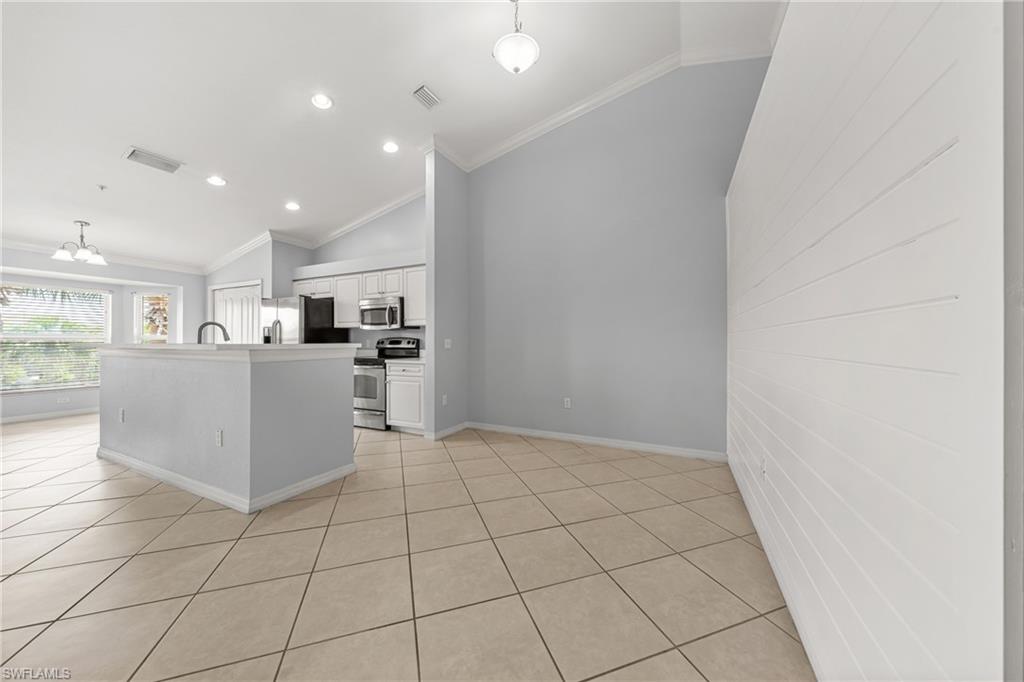 Open-concept kitchen and living area featuring diagonal tile flooring, white cabinetry, stainless steel appliances, a kitchen island with sink, and vaulted ceilings