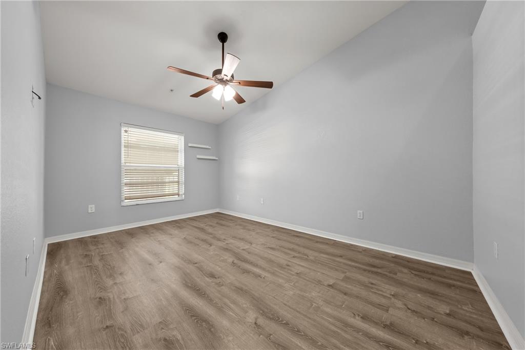 Spacious room featuring wood-finish flooring, a window with horizontal blinds, two wall-mounted shelves, and a ceiling fan with light fixture