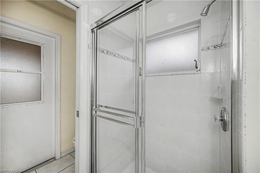 Shower enclosure featuring a framed glass door, white ceramic wall tile, decorative accent tile, a frosted window, and a chrome shower fixture