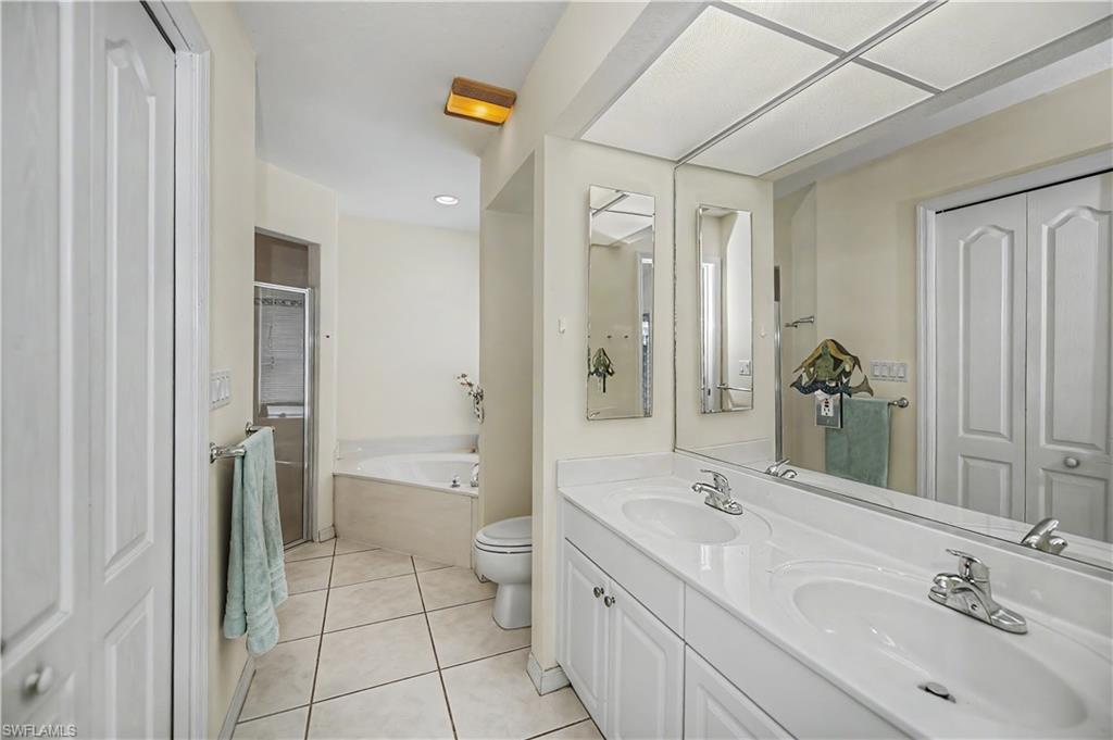 Bathroom featuring a double vanity with white cabinetry, a large mirrored wall, and a tiled floor