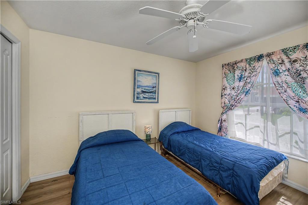Bedroom featuring wood-finish flooring, a ceiling fan, and a window with sheer and patterned drapes