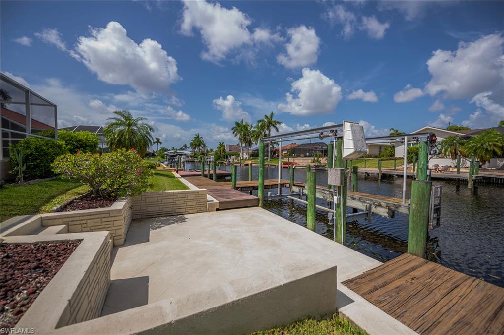 Waterfront property featuring a concrete patio, stone block retaining walls, mature landscaping, a private boat dock, and a boat lift