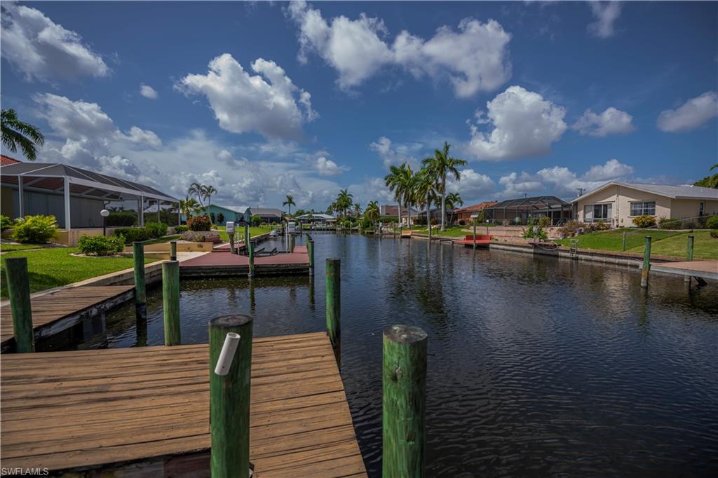 Waterfront canal access featuring a private wooden dock, green pilings, manicured lawns, and mature palm trees