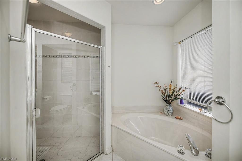 Bathroom featuring a built-in soaking tub, glass-enclosed shower, white tile flooring, and a window with blinds