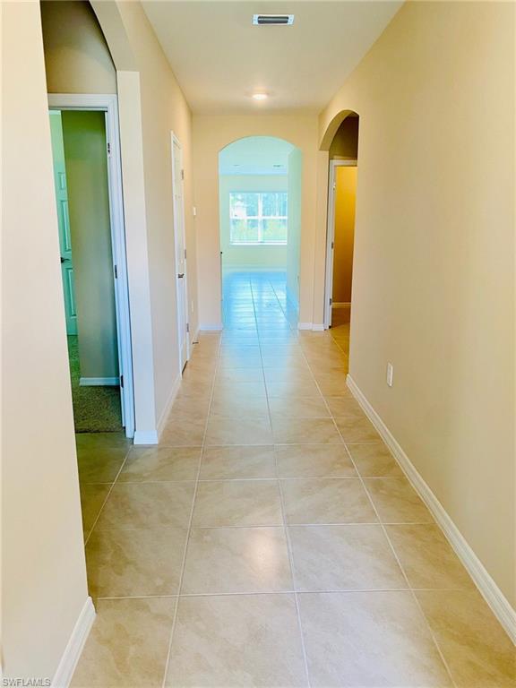 Spacious hallway featuring neutral-toned tile flooring, light beige wall paint, white baseboards, and multiple arched doorways