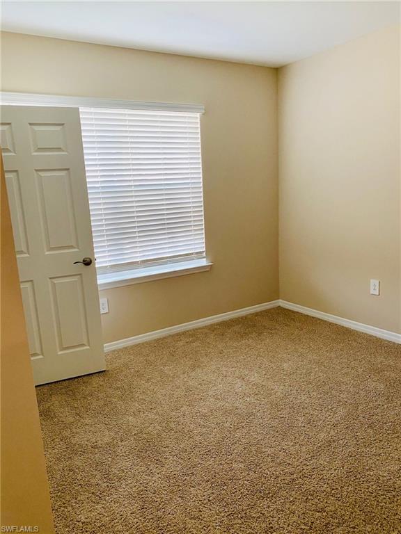 Carpeted room featuring a window with white blinds, a white door with a dark knob, and light beige walls with white trim