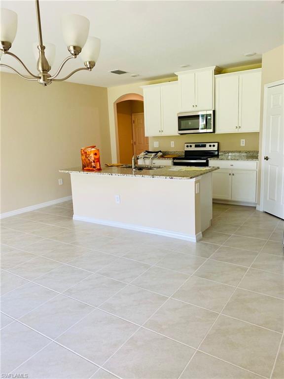 Open-concept kitchen featuring an island with a breakfast bar, granite countertops, white cabinetry, stainless steel microwave, and tile flooring