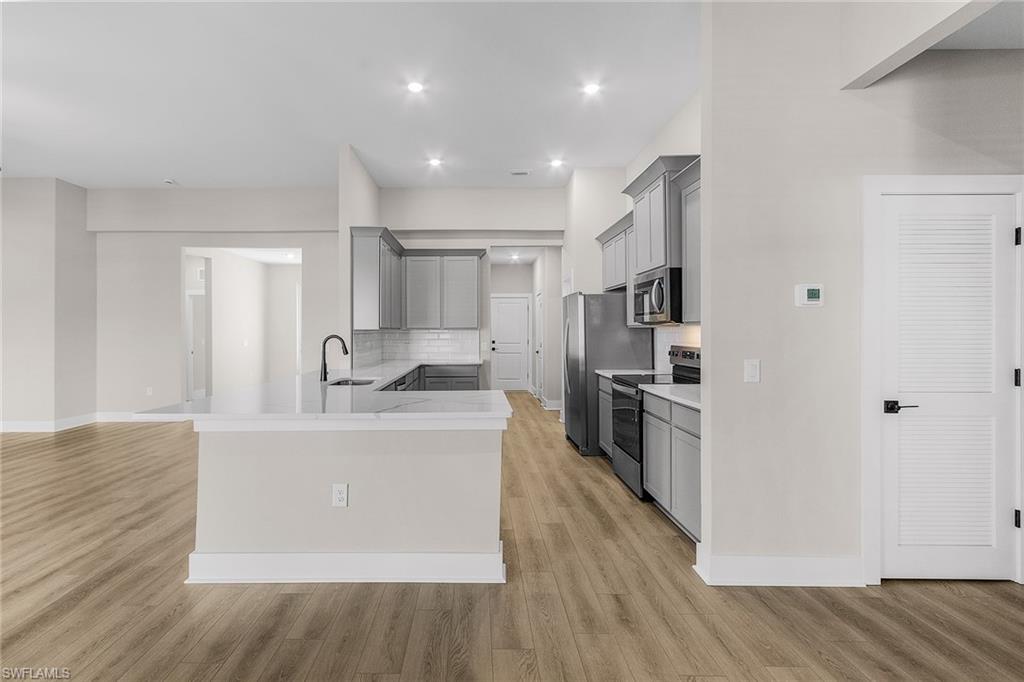 Kitchen with gray cabinetry, backsplash, stainless steel appliances, light wood-style flooring, and recessed lighting