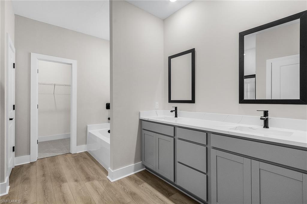 Full bath featuring a walk in closet, light wood-style flooring, a garden tub, and double vanity