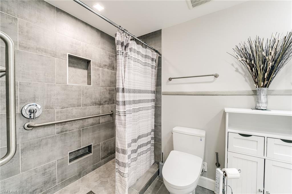 Tiled shower with grab bar, built-in recessed shelving, chrome shower fixtures, and a white toilet