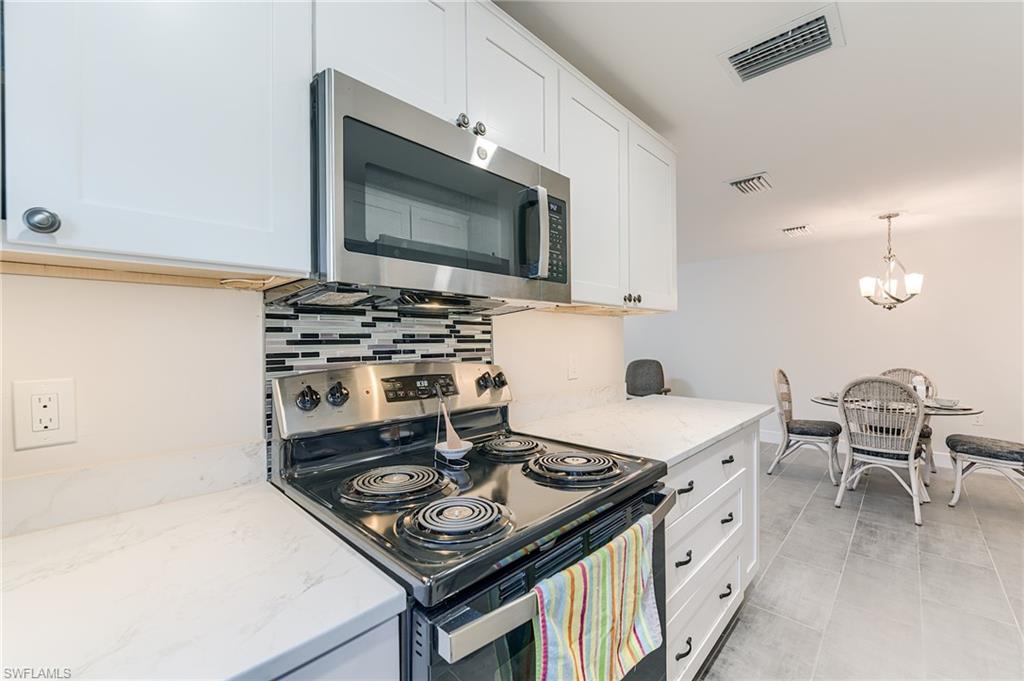 Modern kitchen featuring white cabinetry, quartz countertops, stainless steel gas range with multiple burners, integrated microwave, and mosaic tile backsplash