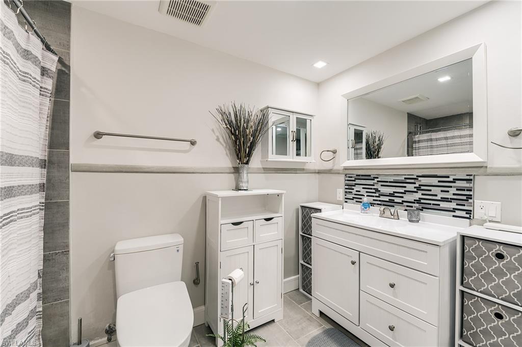 White vanity with integrated sink, mosaic tile backsplash, and large framed mirror