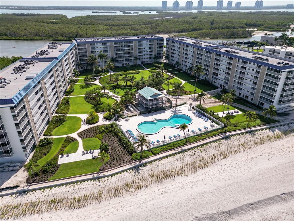 Coastal condominium complex with multiple buildings, an expansive manicured lawn, a kidney-shaped swimming pool, a beachfront location, and a surrounding tropical landscape