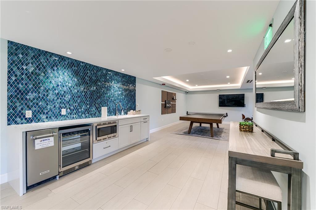 Custom bar area featuring mosaic tile backsplash, built-in beverage refrigerator, microwave, and ample counter space