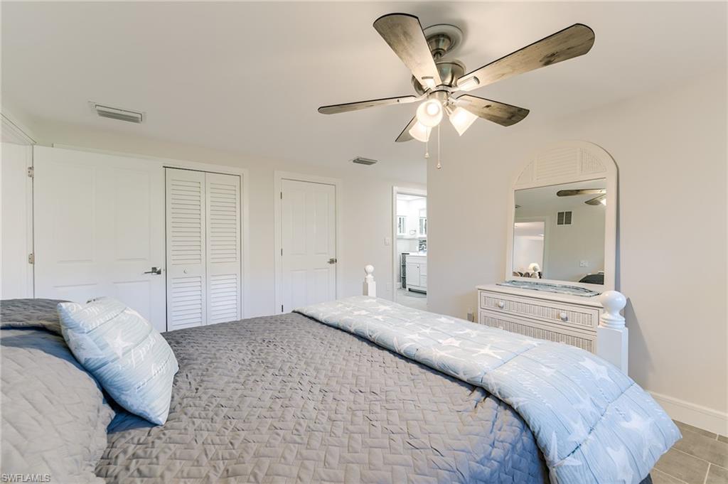 Ceiling fan with light fixture, tile flooring, white interior doors, and louvered closet doors