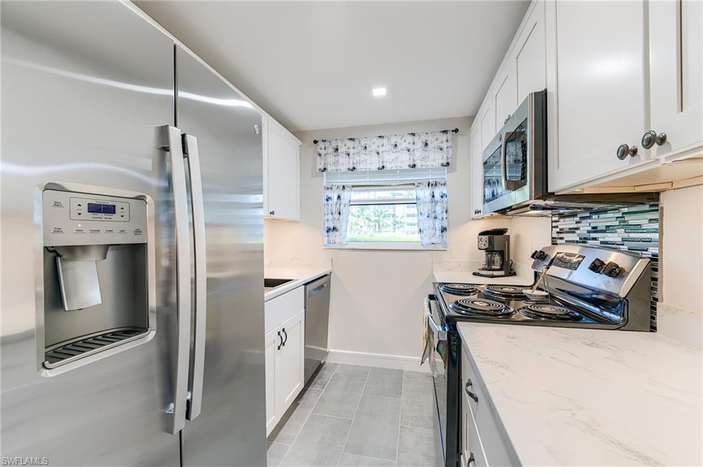 Stainless steel refrigerator with ice and water dispenser, white shaker-style cabinetry, mosaic tile backsplash, and light-toned countertops