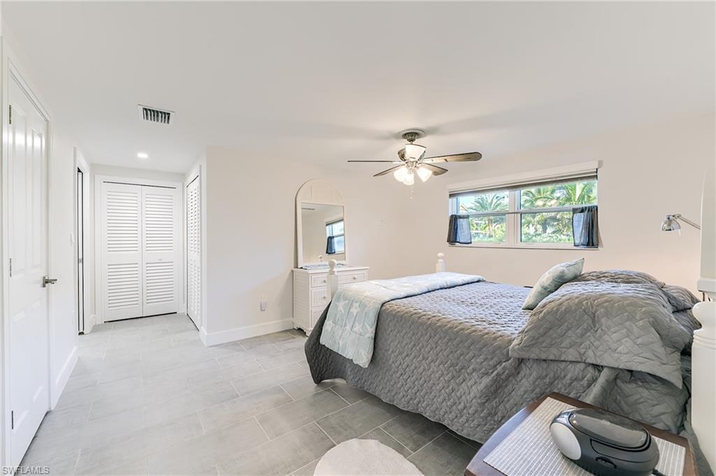 Spacious room featuring light-colored tile flooring, white walls, a ceiling fan, and large windows