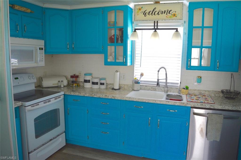 Kitchen featuring bright blue cabinetry with brushed nickel hardware, white appliances, a double basin sink, and a stainless steel dishwasher