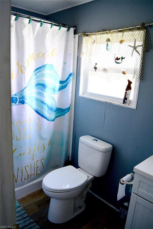 Compact bathroom featuring a white toilet, a window with natural light, and wood-finish flooring