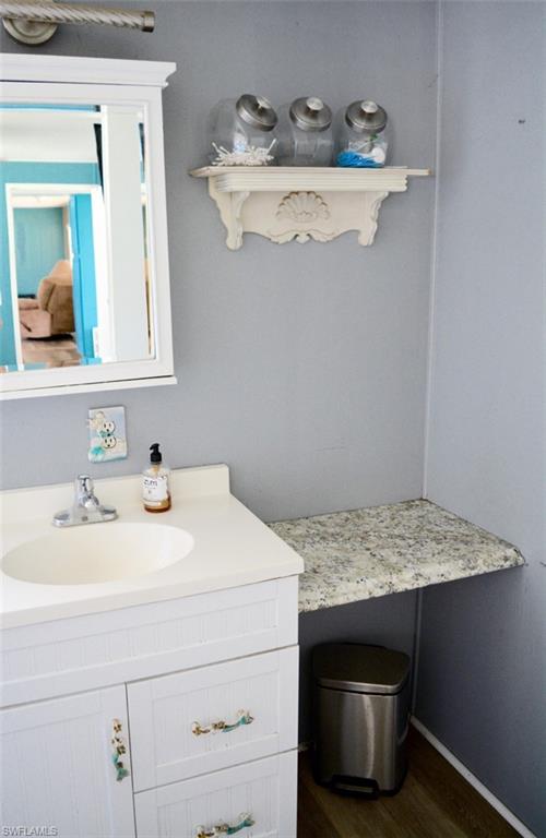 White vanity with a single basin sink and brushed nickel faucet, complete with a white medicine cabinet and a decorative wall shelf