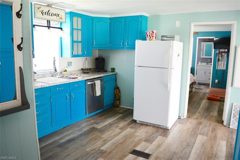Kitchen featuring bright cabinetry, wood-finish flooring, a stainless steel dishwasher, a white refrigerator, and a window with natural light