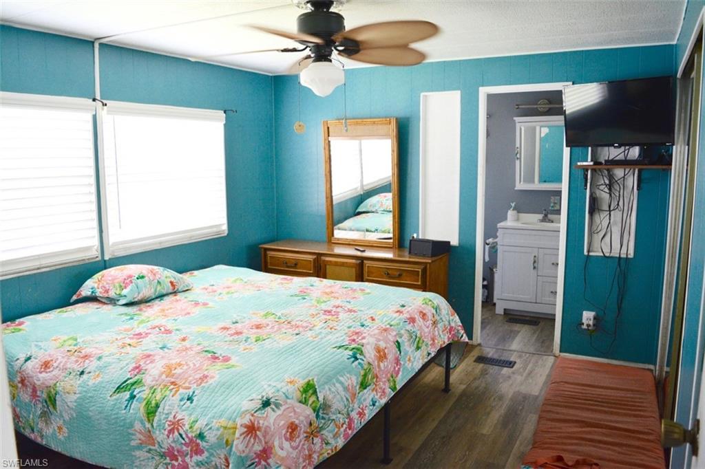Bedroom featuring wood-finish flooring, two windows with horizontal blinds, and a ceiling fan