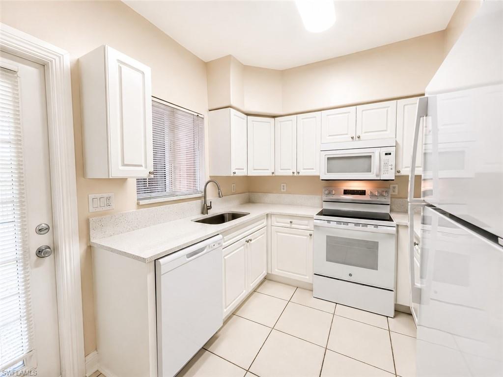 Kitchen featuring white cabinetry, light-toned countertops, a stainless steel sink with a modern faucet, white appliances including a refrigerator and range, and light-colored tile flooring