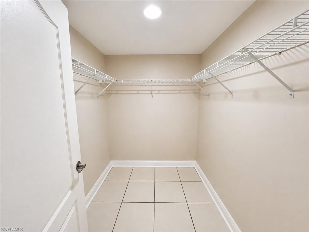 Walk-in closet featuring light beige wall color, white wire shelving, recessed ceiling light, and square tile flooring