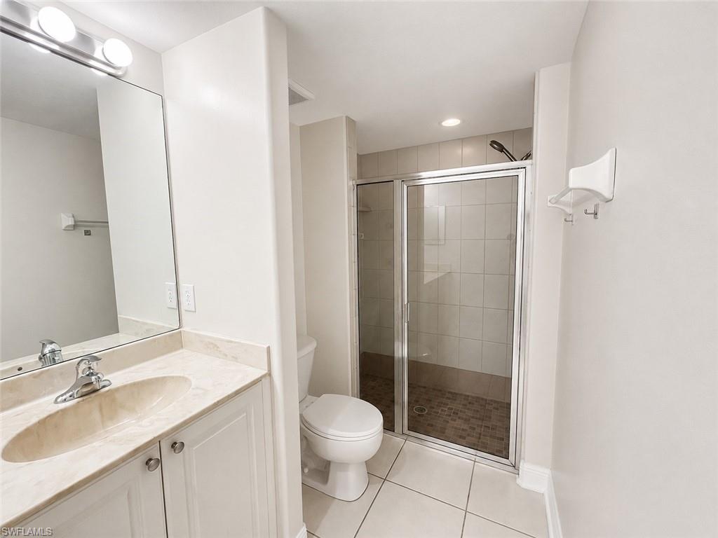 Bathroom featuring a walk-in shower with glass enclosure, white square floor tiles, a single vanity with stone countertop and integrated sink, and white cabinet storage