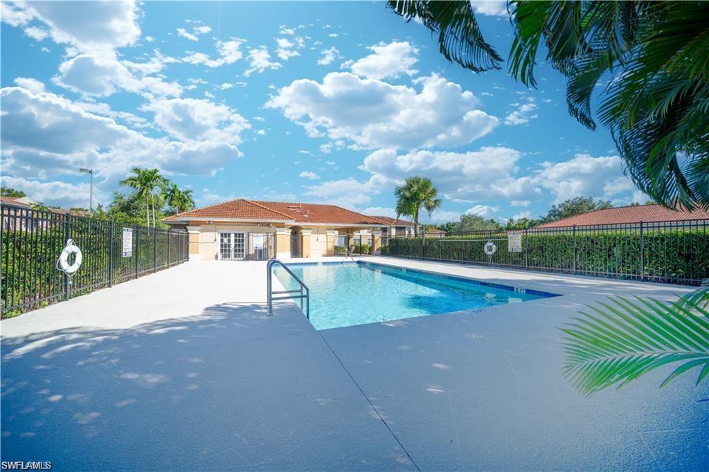 Community swimming pool with a surrounding paved deck, black metal fencing, and lush privacy hedges