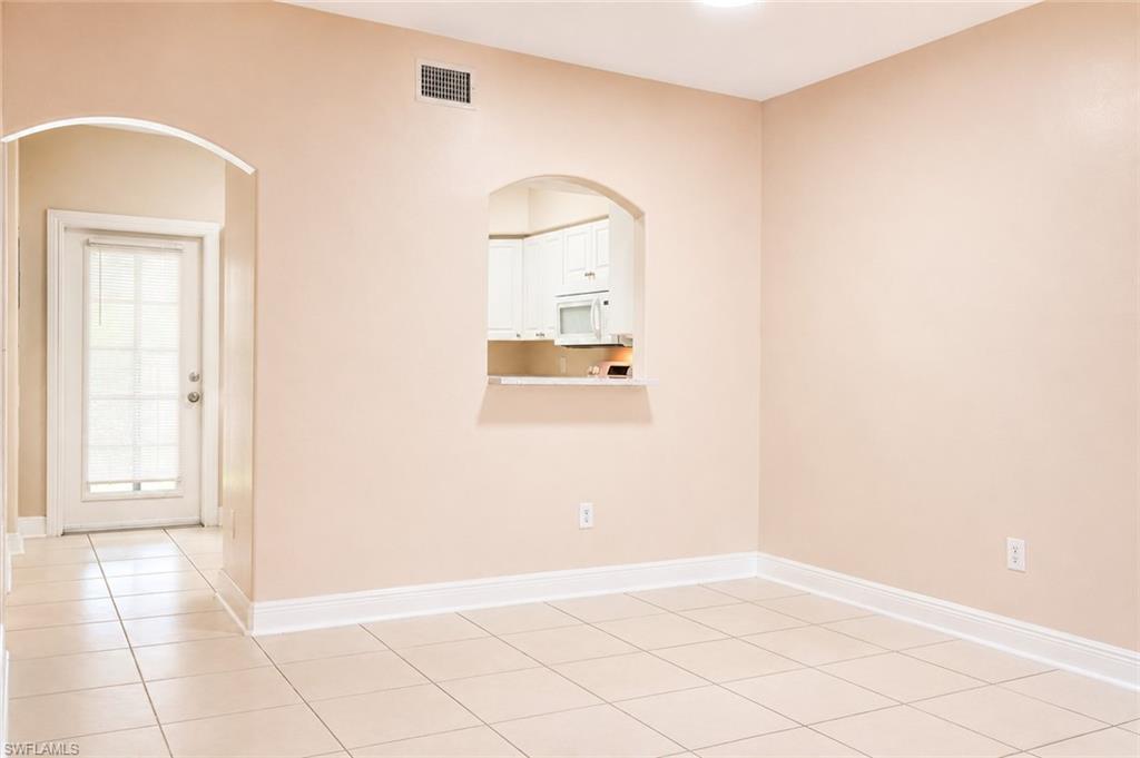 Spacious room with large format tile flooring, a pass-through window to the kitchen, and a white architectural door with glass paneling