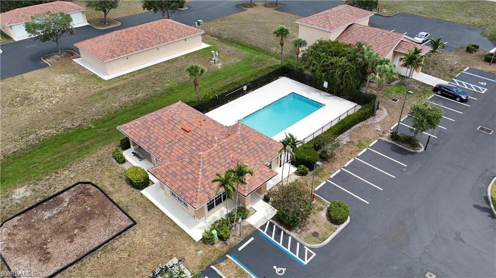 Community swimming pool with surrounding fence and paved deck, accompanied by a clubhouse with a terracotta tile roof, dedicated parking areas, and mature landscaping