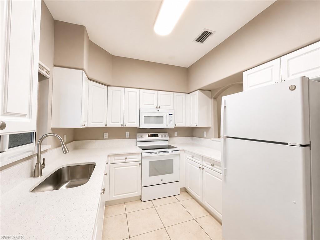 Kitchen with white cabinetry, white appliances, light-toned countertops, and tile flooring