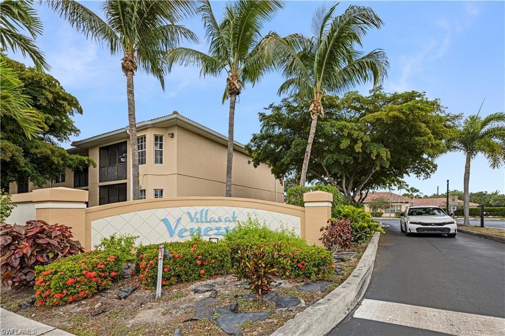 Entry monument with "Villas at Venezia" inscription, tropical landscaping, and a two-story residential building in the background