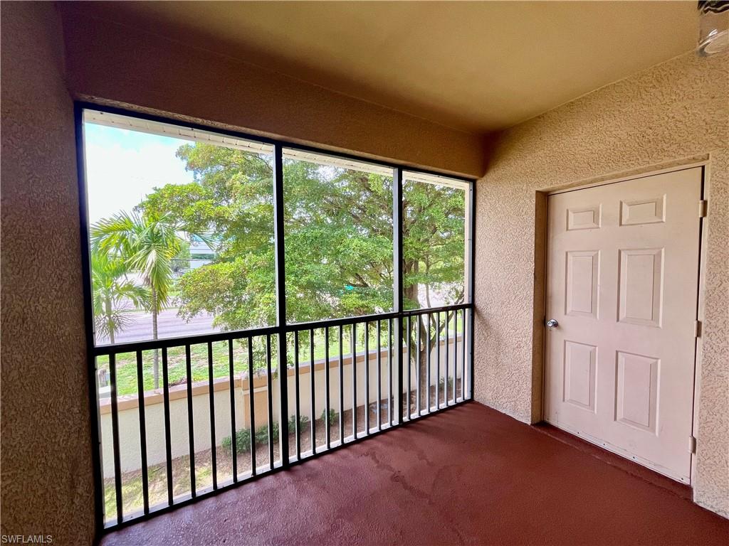 Screened private balcony featuring a textured stucco finish, dark red flooring, and a six-panel door