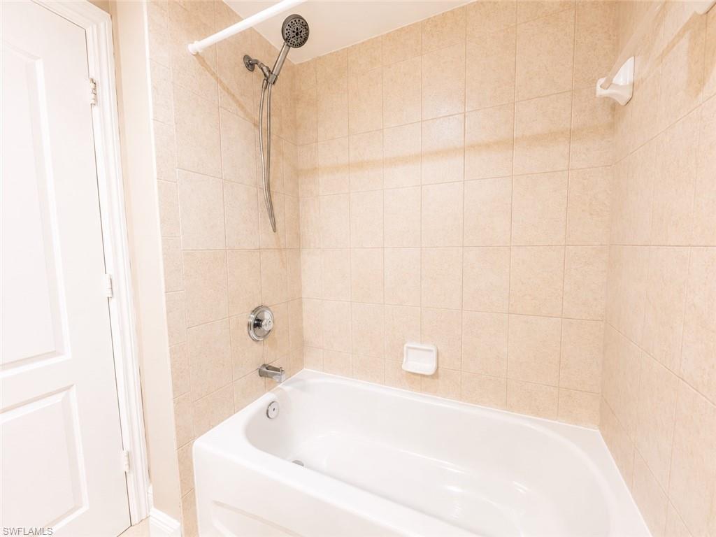 Bathtub and shower combination featuring neutral-toned square wall tiles, a polished chrome faucet, and a handheld showerhead