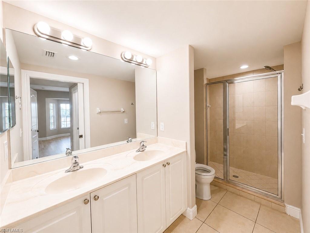 Spacious bathroom featuring a double vanity with ample counter space, dual sinks, a large wall-mounted mirror, and a glass-enclosed shower with tiled walls