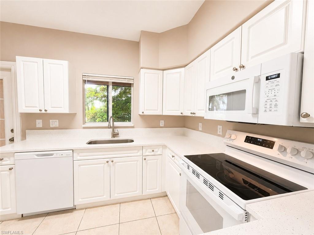 Kitchen featuring white cabinetry with brushed nickel hardware, light-toned countertops, tile flooring, and integrated white appliances including a built-in microwave and glass cooktop