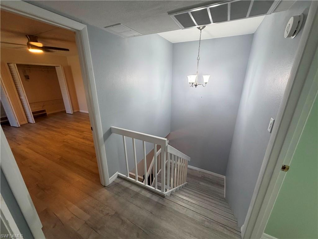 Stairwell featuring light gray walls, white balusters, wood-finish flooring, and a three-light chandelier