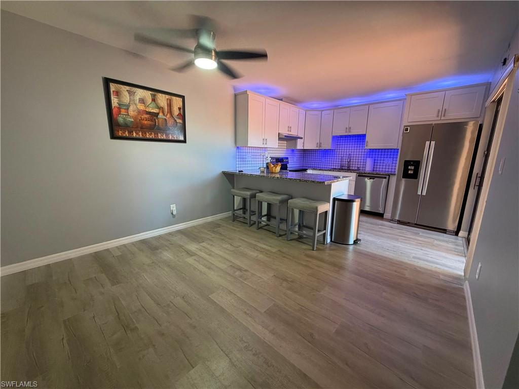 Open-concept kitchen and dining area featuring light wood-finish flooring, white baseboards, and a modern ceiling fan