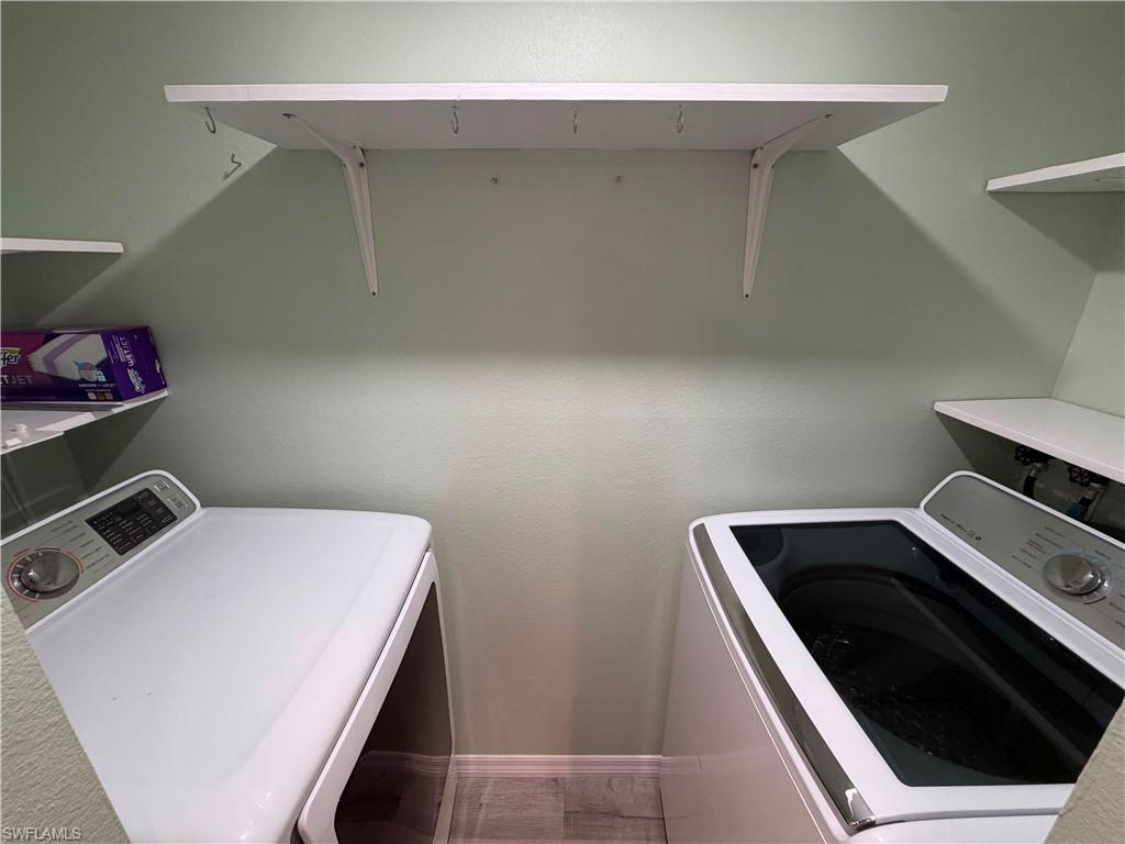 Dedicated utility space featuring light green walls, a top-mounted white shelf with hooks, and wood-finish flooring