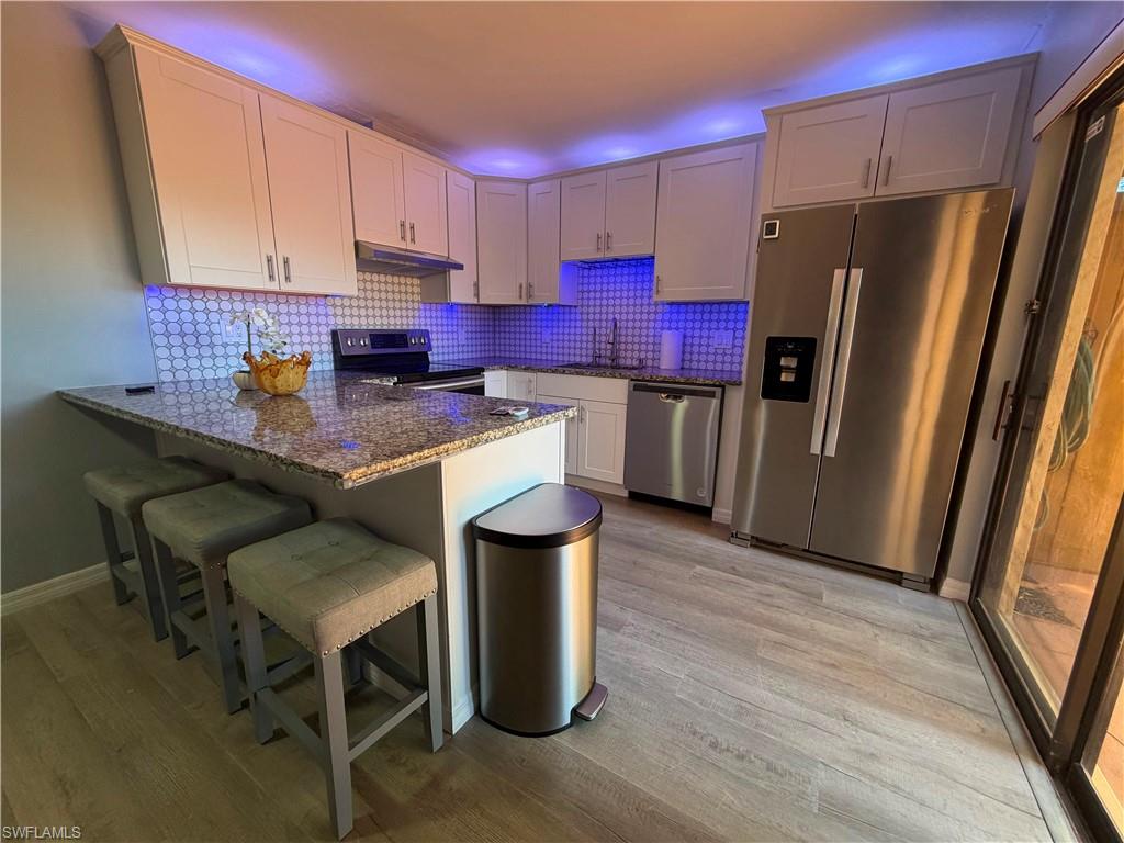 Kitchen featuring white shaker cabinetry, granite countertops, tile backsplash, stainless steel appliances, and wood-finish flooring