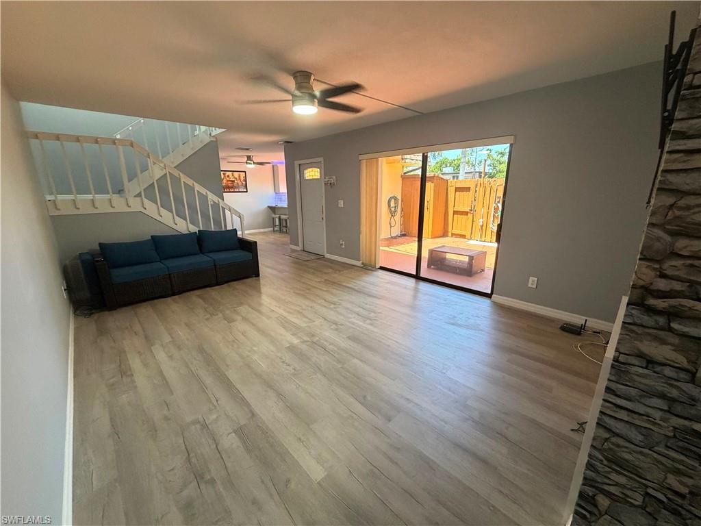 Spacious living area featuring light wood-finish flooring, a ceiling fan with integrated lighting, and a stone-clad accent wall
