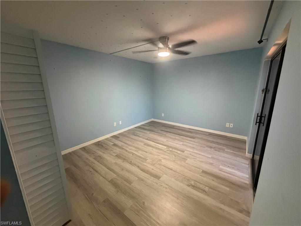 Spacious room featuring light blue walls, wood-finish flooring, white baseboards, and a ceiling fan with integrated lighting