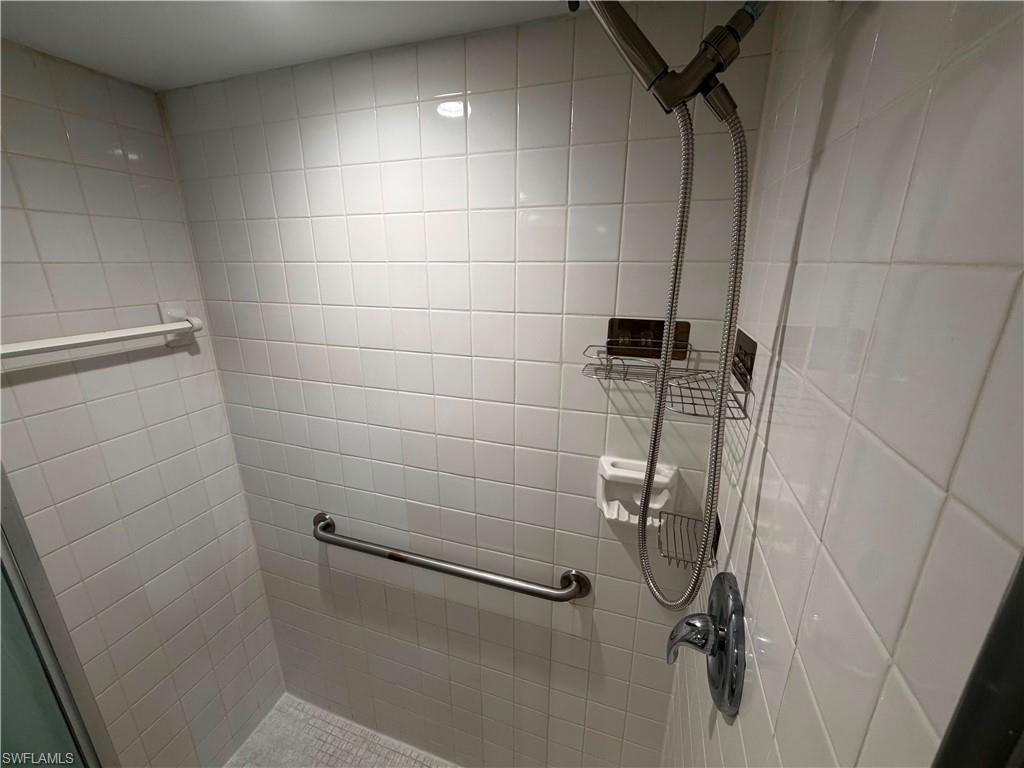 Shower enclosure with white square tile, a handheld showerhead, a chrome grab bar, and built-in shelving
