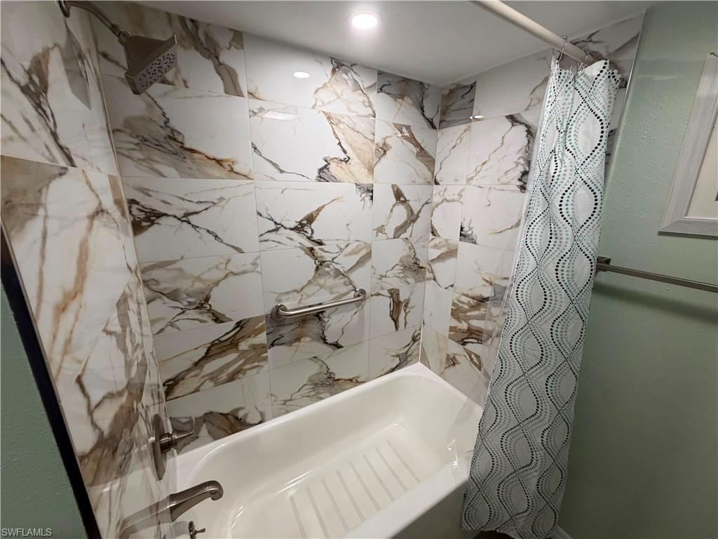 Bathtub with white and brown veined tile surround, brushed nickel showerhead, and wall-mounted grab bar